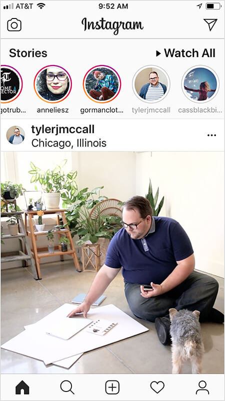 Tyler J. McCall has noticed that the Instagram algorithm seems to show a view more of an account’s content in the feed if you watch or interact with the account’s Instagram story and vice versa. A user’s Instagram home screen shows a post from Tyler after the user has watched his story. The Instagram feed image shows Tyler sitting on the floor with large sheets of white paper and a notebook. A small black and tan dog faces Tyler. Lots of green plants on ladders are in the background.