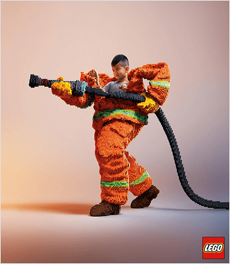 This is a photo from a LEGO ad that shows a young Asian boy inside a firefighter uniform made of LEGOs. The uniform is orange with a neon green stripe around the cuffs of the coat and pants. The firefighter is standing with one foot back and holding a firehose, also made of legos. The boy’s head appears out of the top of the uniform, which is much larger than he is and stops around the shoulders. The photo was taken against a plain neutral background. The LEGO logo appears in a red box in the lower right. Talia Wolf says LEGO is a great example of a brand that uses emotion in advertising.