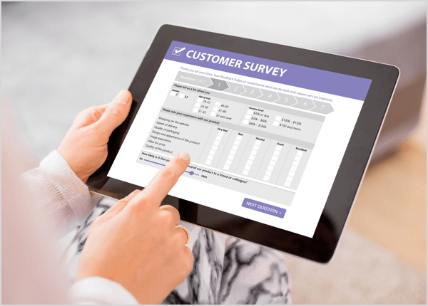 This is a photo of a tablet showing a customer survey on-screen. The hands of a white person are holding the tablet and tapping responses.