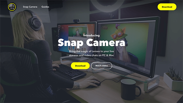 This is a screenshot of the Snap Camera website. In the page background a woman sits at a desktop computer with headphones on, using an augmented reality lens to make it seems like she’s wearing a silly, cartoonish hat. The white text in the center of the page says “Bring the magic of Lenses to your live streams and video chats on PC and Mac.” A yellow button is labeled Download.